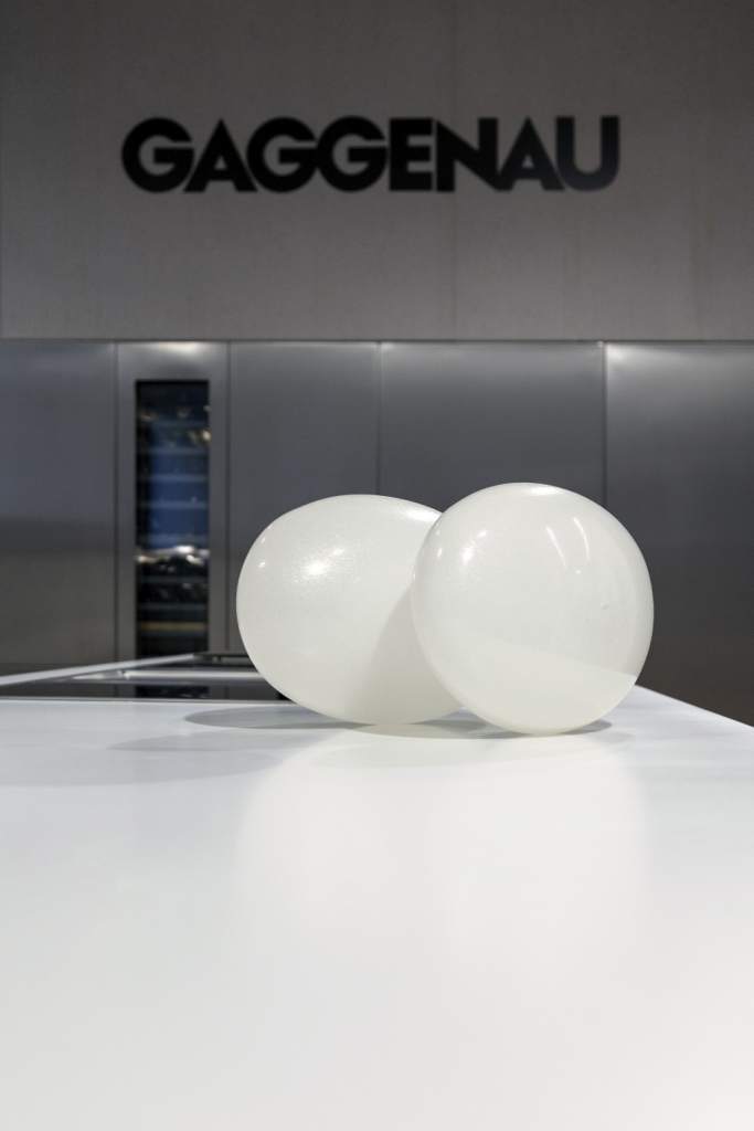 fotografia, interno, colori, uova di vetro bianche appoggiate, sfondo pareti grigie scritta "Gaggenau", mostra "ab - L'Essenza dell'Assenza"