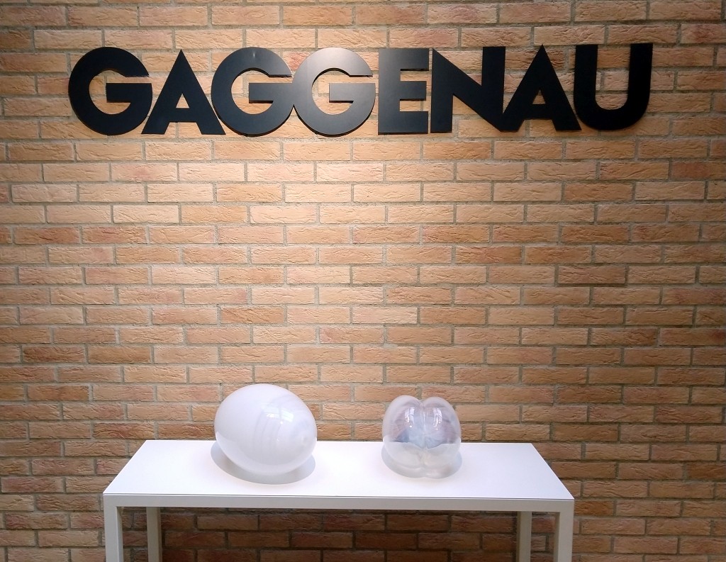 fotografia, colori, interno, due opere in vetro appoggiate su tavolo bianco, sfondo parete mattoni scritta "Gaggenau", mostra "ab - L'Essenza dell'Assenza"