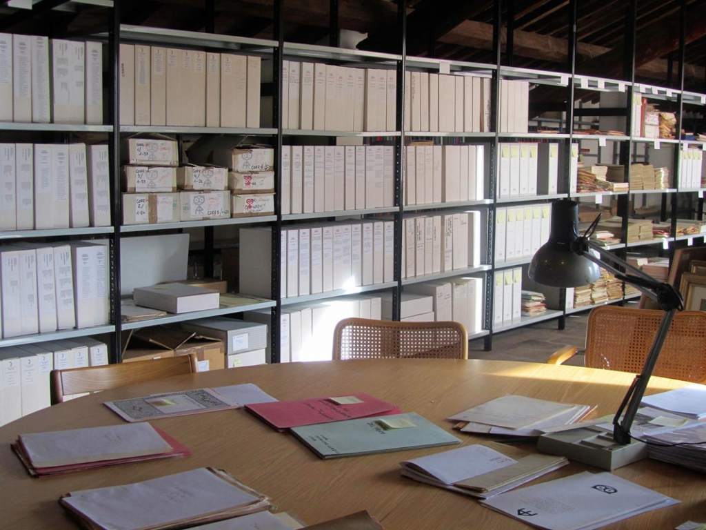 fotografia, colori, interno, tavolo con documenti e lampada, sfondo scaffale archivio, Fondazione Ragghianti Lucca