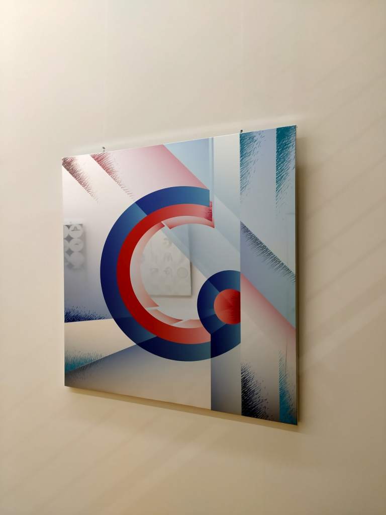 fotografia, colori, interno, opera d'arte di Lorenzo Marini, lastra di acciaio specchiato con stampata lettera G in rosso e blu, su parete bianca