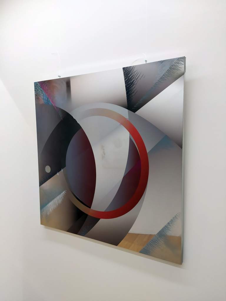 fotografia, colori, interno, opera d'arte di Lorenzo Marini, lastra di acciaio specchiato con stampata lettera O in rosso e grigio, su parete bianca