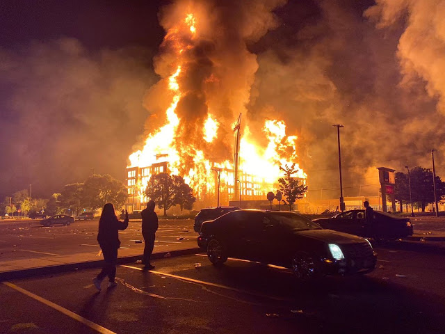 Caserma della polizia in fiamme a Minneapolis, due manifestanti passano davanti per la morte di George Floyd