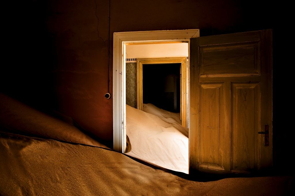 Interno di una casa a Kolmanskop in primo piano una porta sommersa di sabbia