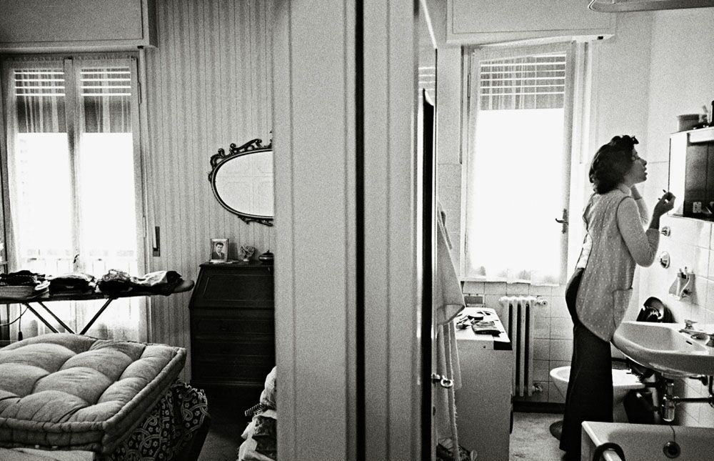 fotografai epoca, bianco e nero, appartamento e giovane donna che si trucca in piedi allo specchio