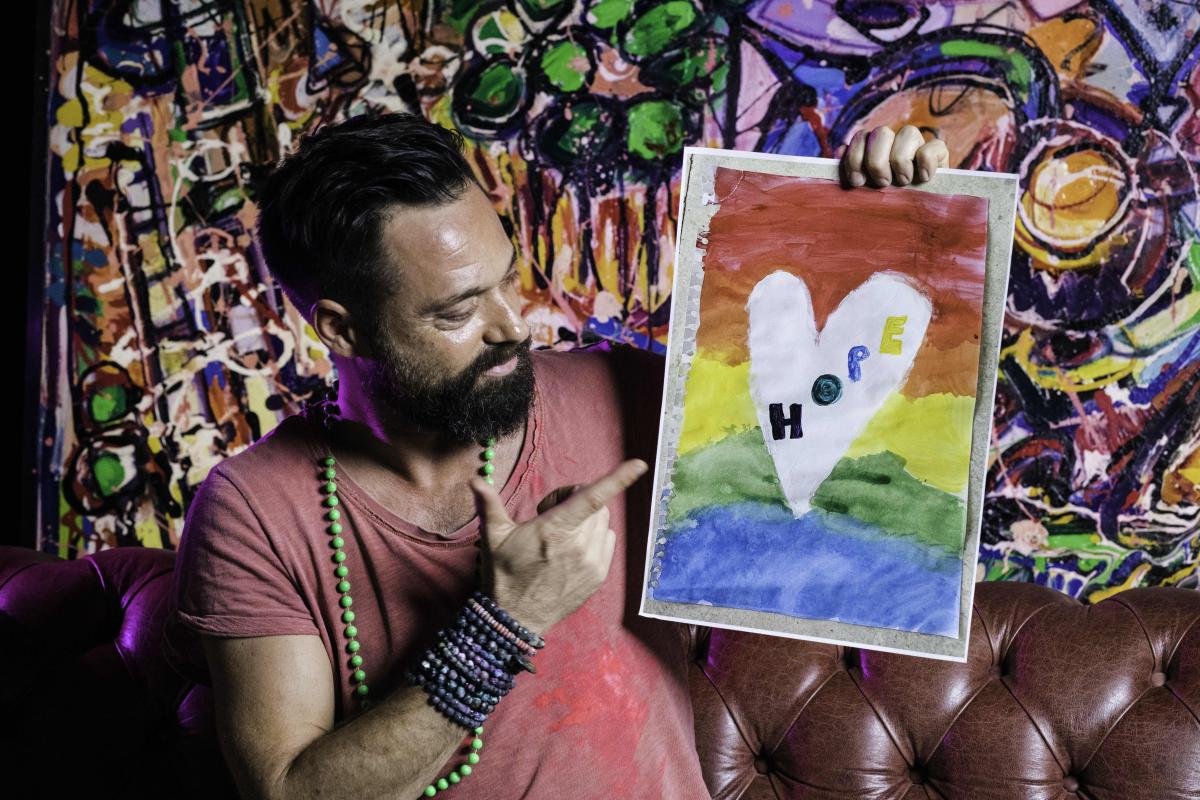 artista Sacha Jafri con in mano un disegno di un cuore con scritto al centro hope