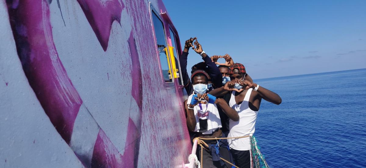 una foto di alcune persone sulla barca Louise-Michel che fanno con le mani il simbolo del cuore