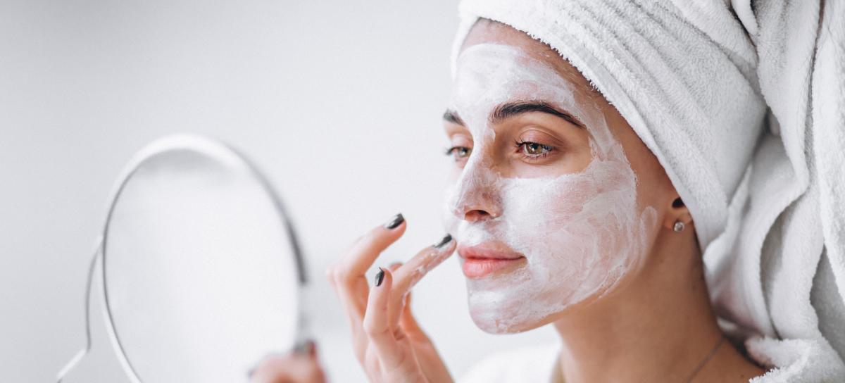 in primo piano il viso di una donna con una maschera di bellezza mentre di guarda allo specchio