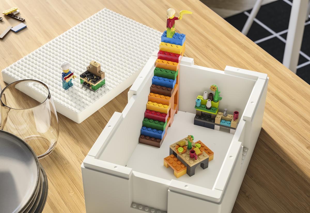 vista dall'alto di una scatola BYGGLEK collezione tra IKEA e LEGO, una scaletta di lego con in cima un personaggio della lego, dentro la scatola un tavolo di lego e sul lato una cucina di lego