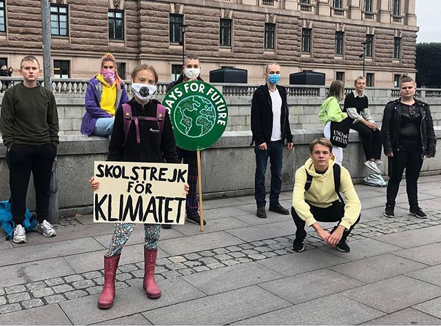 Greta Thunberg con in mano il cartello iconico contro il cambiamento climatico davanti al parlamento svedese, intorno a lei altri ragazzi