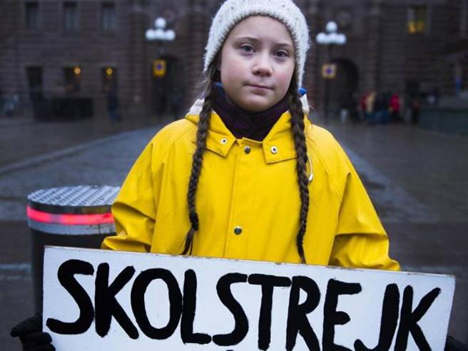 Greta Thunberg in una delle sue prime immagini con l'impermeabile giallo, le trecce e il cartello iconico